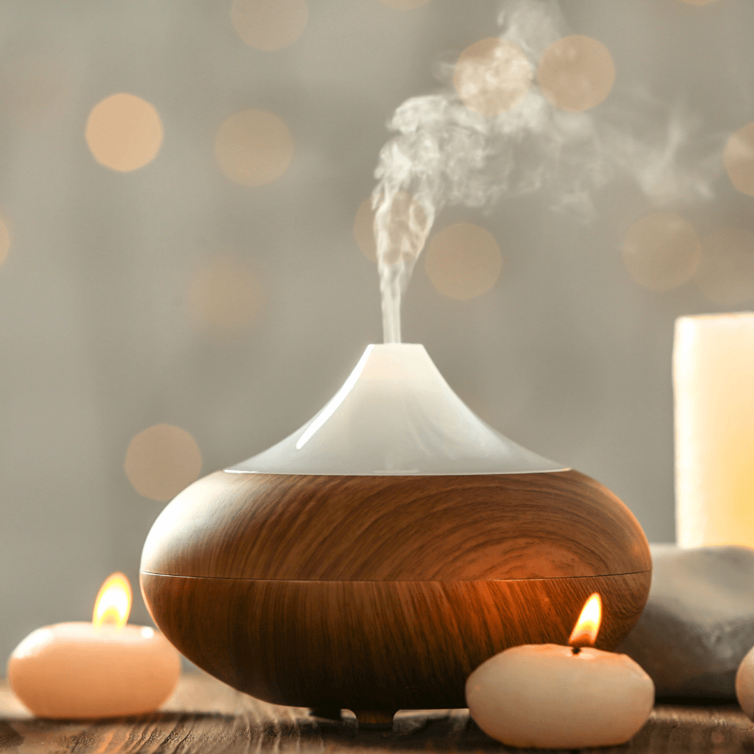 Aromatherapy diffuser releasing a plume of mist beside lit candles on a wooden table