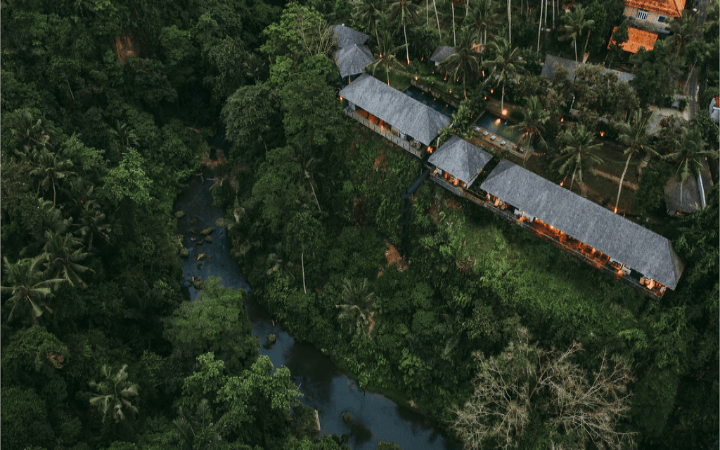 Aerial view of villa roofs set in dense jungle beside a river in the Ubud highlands